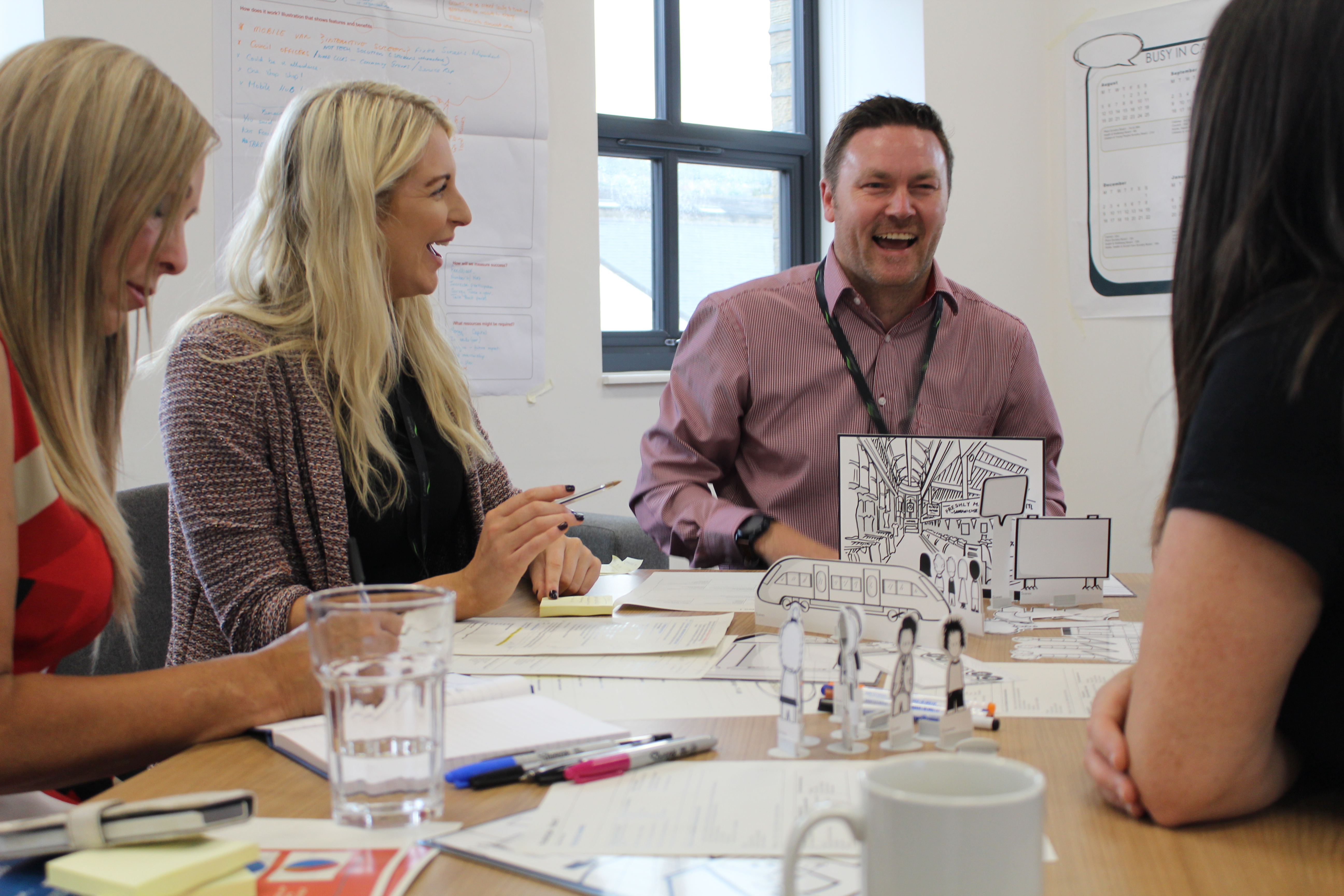 People laughing sat around a table with papers and prototyping tools on it