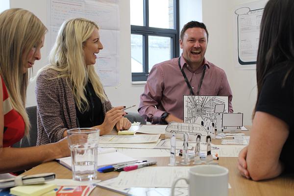 A small group laughing together around a table in a workshop.